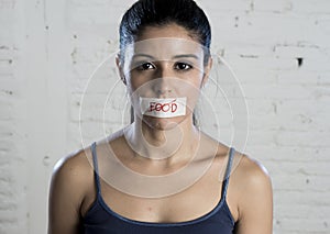 Close up face of young beautiful sad latin woman with mouth sealed on stick tape with the text no food