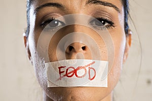 Close up face of young beautiful sad latin woman with mouth sealed on stick tape with the text no food