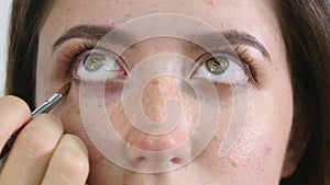 Close up of a face of young professional female photomodel during make-up process at beauty shop. Young visagiste is