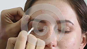 Close up of a face of young professional female photomodel during make-up process at beauty shop. Young visagiste is