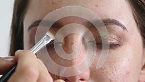 Close up of a face of young professional female photomodel during make-up process at beauty shop. Young visagiste is