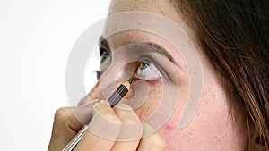 Close up of a face of young professional female photomodel during make-up process at beauty shop. Young visagiste is