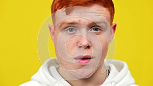 Close-up face of young redhead man with problematic skin posing at yellow background. Headshot portrait of Caucasian
