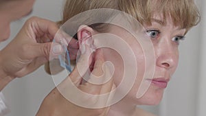 Close-up face of young woman with blurred doctor inserting needles into her ear. Side view portrait of blond beautiful