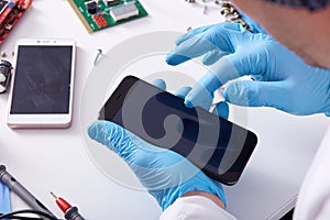 Close up faceless portrait of person`s hand in blue rubber gloves fixing damaged screen of mobile phone, unknown person sitting a