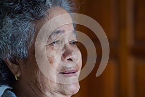 Close-up of facing a senior woman smiling and looking away while sitting on a chair in a living room. Concept of aged people