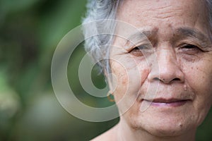 Close-up of facing a senior woman smiling and looking at the camera while standing outdoors. Space for text.