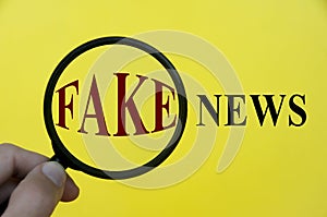 Close-up at fake news text through magnifying glass on yellow cover background. Fake news concept