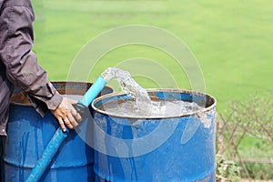 Close up farmer hand hold pipe of water to put into blue buckets in garden.
