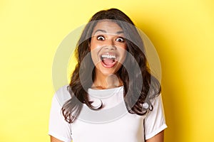 Close-up of fascinated african-american girl, open mouth and looking amazed at something cool, standing over yellow