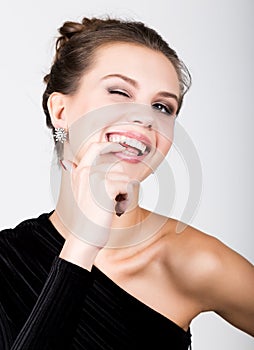 Close-up fashion photo of young lady in elegant black dress, playful woman raised index finger to his lips