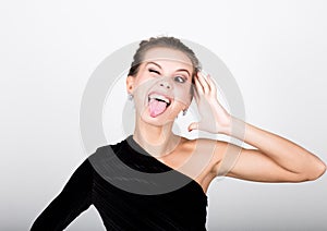 Close-up fashion photo of young lady in elegant black dress, playful woman shows tongue