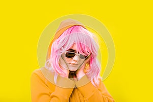 Close up fashion portrait young beautiful woman in hoodie and glasses. Alternative funky girl with pink hair on yellow