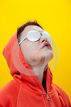 Close up fashion portrait young beautiful woman in hoodie and white glasses. Alternative funky girl on a bright yellow