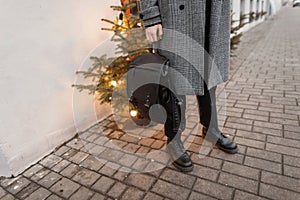 Close-up of a fashionable black leather backpack in the hands of a stylish man in an elegant plaid coat with boots in pants near a