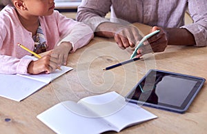 Close Up Of Father Helping Daughter With Home Schooling Sitting At Table With Digital Tablet