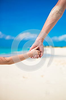 Close up of father and little daughter holding each other hands at beach