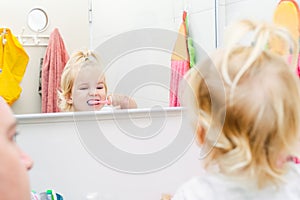 Close up father and little toddler daughter brushing her teeth and looking in the mirror in the bathroom. Reflection in the mirror