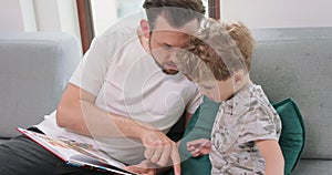 Close up of father and son are spending time together at home by reading a book on the sofa and compose a story from