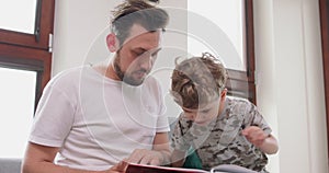 Close up of father and son are spending time together at home by reading a book on the sofa and compose a story from