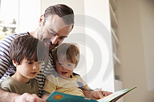 Close Up Of Father And Sons Reading Story At Home Together