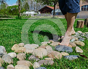 Close-up on the feet of a Caucasian man engaged in a barefoot path: a stretch of rounded stones follows wooden trunks on a meadow