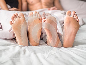 Close up of the feet of a couple on the bed. Loving couple is lying on bed under blanket