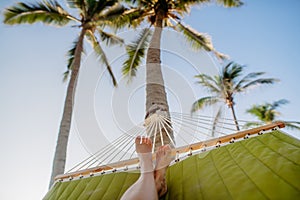 Close-up of feet in hammock, palm trees in background, vacation concept.