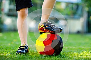 Close-up of feet of kid boy with football and soccer shoes in German national colors - black, gold and red. World or