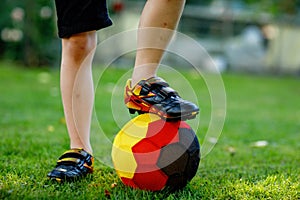 Close-up of feet of kid boy with football and soccer shoes in German national colors - black, gold and red. World or