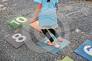 Close-up feet of little girl play jumping on colourful hopscotch playground markings numbers on stone at pavement