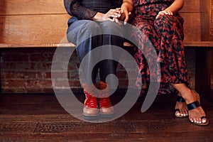 Close Up On Feet Of Same Sex Female Couple Holding Hands Sitting On Bench Together