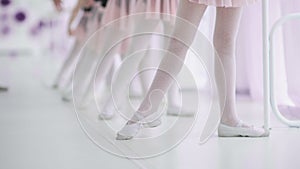 Close up feet of unrecognizable little girls in white socks and ballet shoes, their ballet teacher correcting them