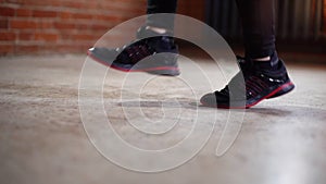 Close-up feet of unrecognizable young female boxer in black sneakers jumping on skipping rope during workout training.