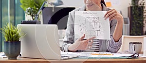 Close Up Of Female Architect In Office Sitting At Desk Showing Plans For New Building On Video Call
