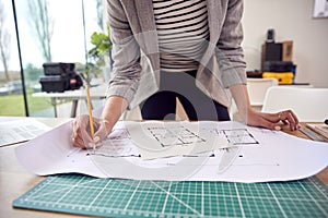 Close Up Of Female Architect Standing Working In Office Studying Plans For New Building