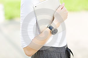 Close-up of female arm wearing a watch and carrying a digital tablet outdoors.