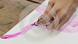 Close up of female artist paints an abstract picture, he uses pink paint fron tube on wet canves