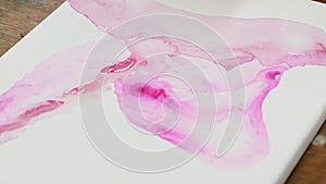 Close up of female artist paints an abstract picture, he uses pink paint fron tube on wet canves