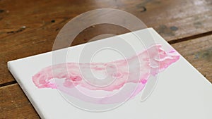 Close up of female artist paints an abstract picture, he uses pink paint fron tube on wet canves and distribute it with