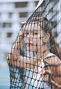 Close up of a female athlete leaning against a tennis net. Young hispanic tennis player posing on a tennis court