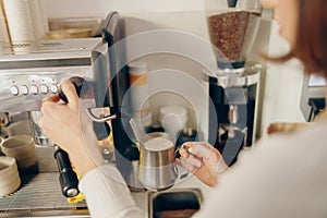 Close up of female barista froths milk on a coffee machine for making cappuccino or latte photo