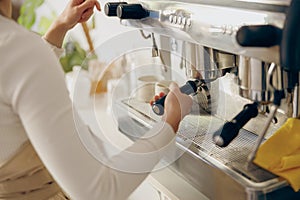 Close up of female barista making coffee in a coffee machine while working in cafe