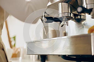 Close up of female barista making coffee in a coffee machine while working in cafe