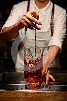 close-up of female bartender gently stirring with spoon cocktail in transparent mixing cup