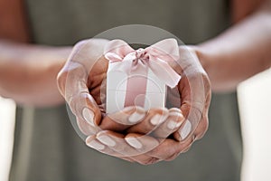 Close up of female black hands holding a small gift wrapped with pink ribbon