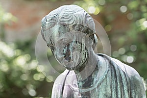 Close up of a female bronze statue of a woman with short hair with cross and cardigan in a park, Germany