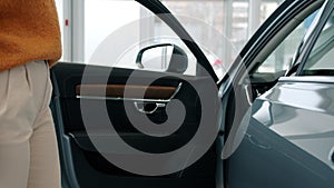 Close-up of female buyer opening car door choosing automobile in dealership