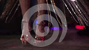 Close-up of female Caucasian feet in gold high heel shoes dancing in night club. Legs of young beautiful woman moving on