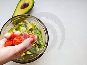 Close up of female chef hand putting Feta cheese cubes on greek vegan tomato salad with olives and lettuce leaves. The concept of